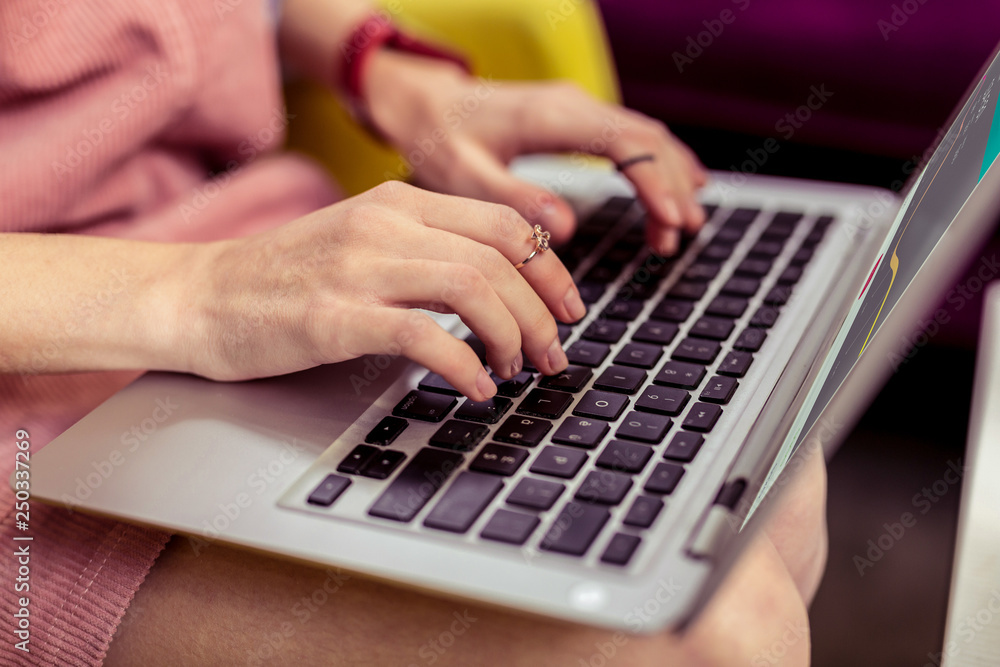Young girl with golden accurate jewelry typing on her laptop keyboard Young girl with golden accurate jewelry typing on her laptop keyboard