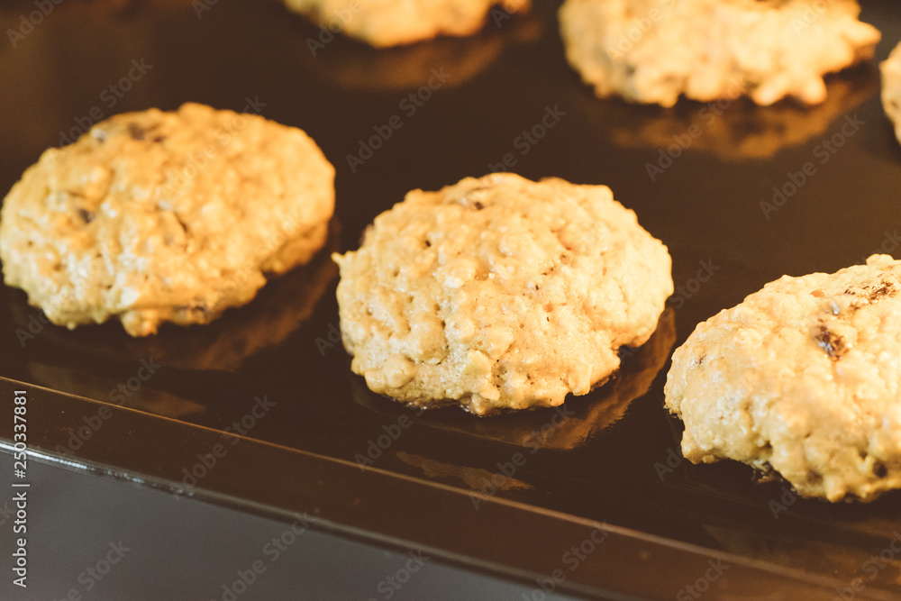 Closed up of hot baking oatmeal raisin cookies on black plate pan in the oven, using raisin and oat for main ingredient Closed up of hot baking oatmeal raisin cookies on black plate pan in the oven, using raisin and oat for main ingredient
