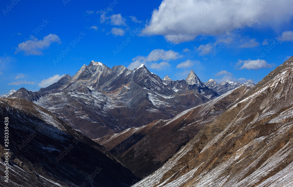 Landscape Photo - Jagged Mountain Peaks in the distance, Four Girls Mountain National Park in Sichuan Province, China. Blue Sky, white puffy clouds, Snow Covered High Altitude Mountains. Siguniangshan