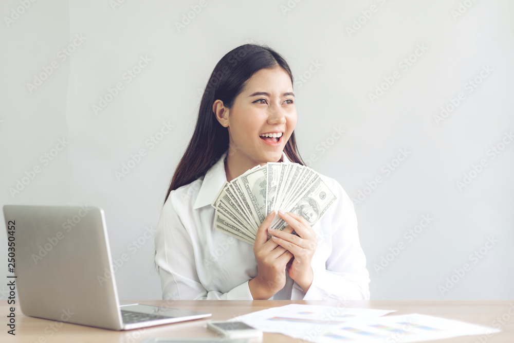 Successful beautiful Asian business young woman holding money US dollar bills in hand on office desk, business concept Successful beautiful Asian business young woman holding money US dollar bills in hand on office desk, business concept