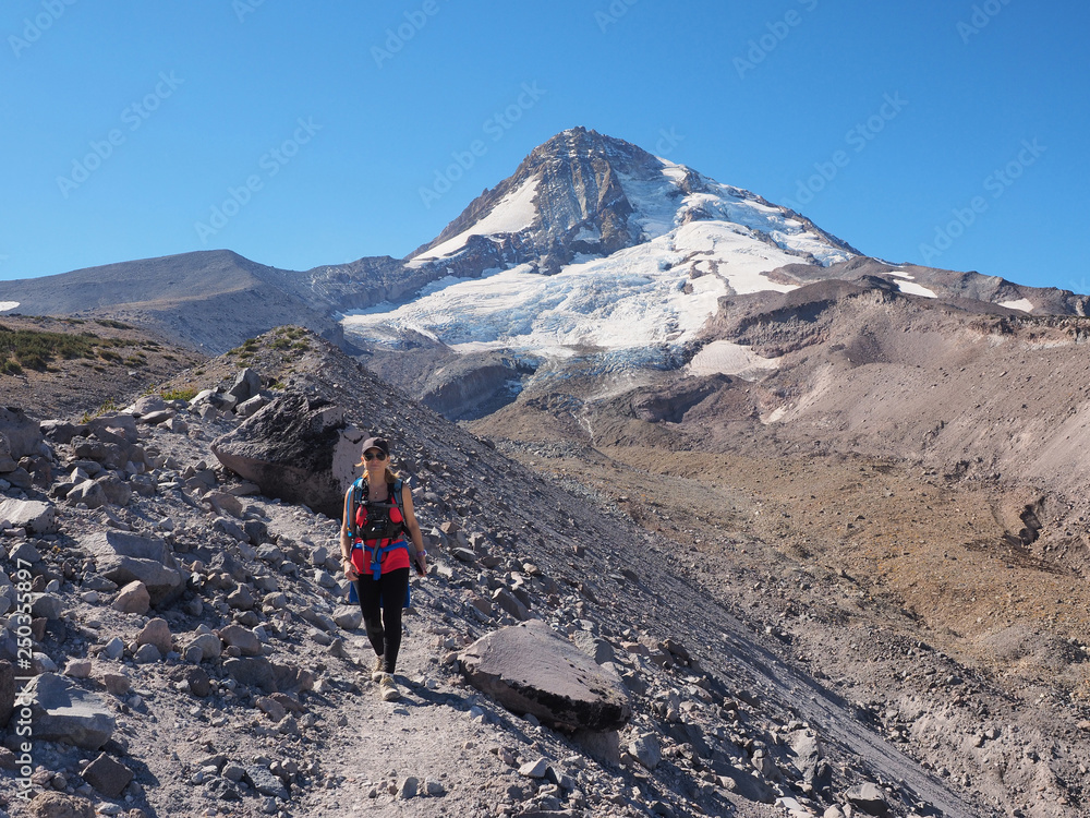 Woman hiking on the Timberline Trail on Mount Hood, Oregon, enjoying views of the volcano's north face and Eliot Glacier on an exceptionally clear day