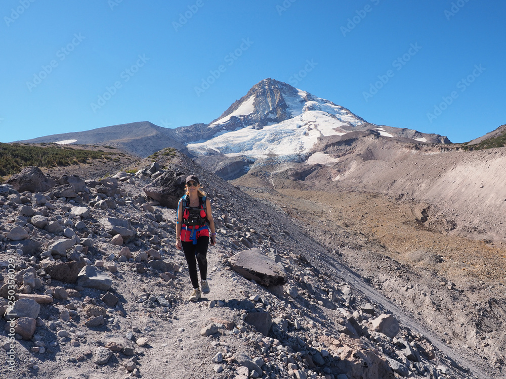 Woman hiking on the Timberline Trail on Mount Hood, Oregon, enjoying views of the volcano's north face and Eliot Glacier on an exceptionally clear day