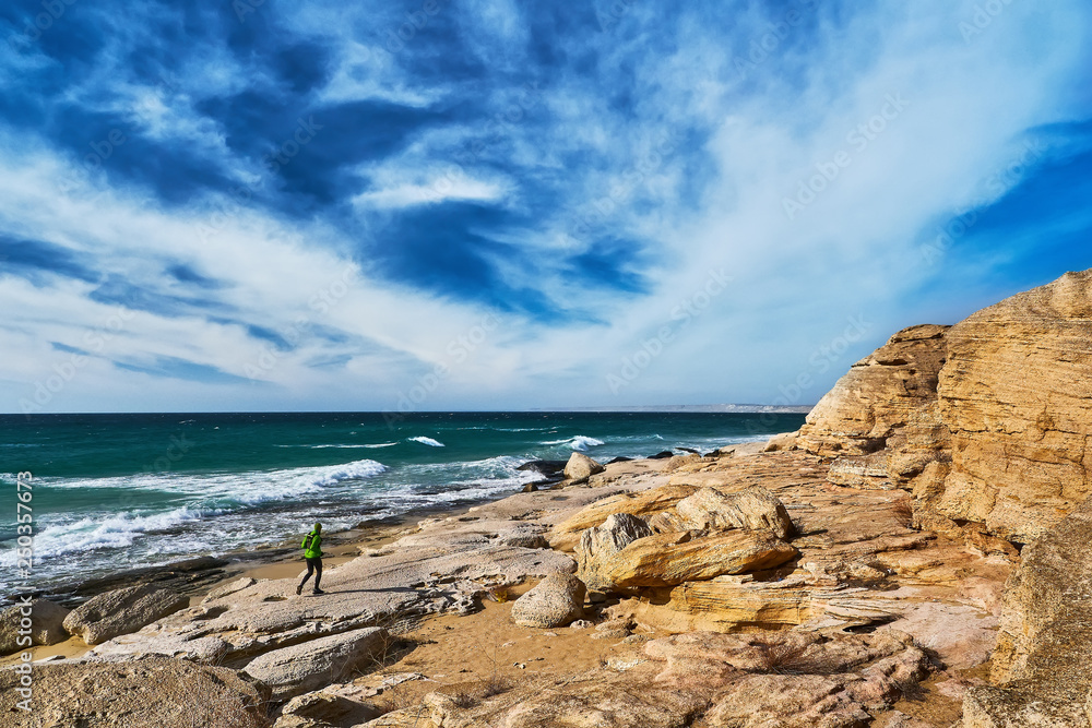 Trail running along the seashore. A man runs along the seashore among the stones on a sunny day Trail running along the seashore. A man runs along the seashore among the stones on a sunny day