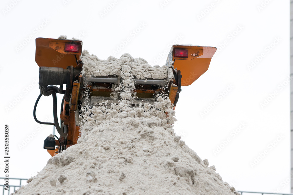 Snow removal from the road. Snow is dumped from the snowplow conveyor into the body of the truck. Snow removal from the road. Snow is dumped from the snowplow conveyor into the body of the truck.