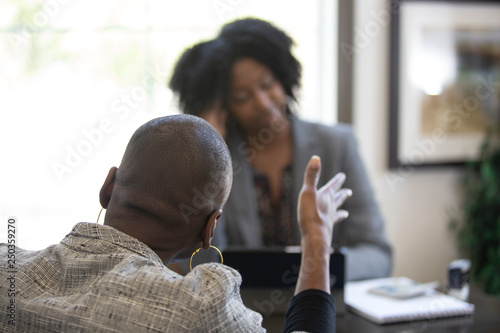 Black female client is upset at tax preparer or CPA accountant in an office.  The image can also depict a manager angry at a secretary.