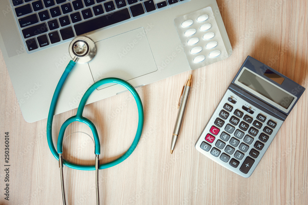 Stethoscope and Calculator on Doctor Office Table., Table Workspace Desktop for Examining Patient Health., Business Healthcare Insurance and Medicine Concept. Stethoscope and Calculator on Doctor Office Table., Table Workspace Desktop for Examining Patient Health., Business Healthcare Insurance and Medicine Concept.
