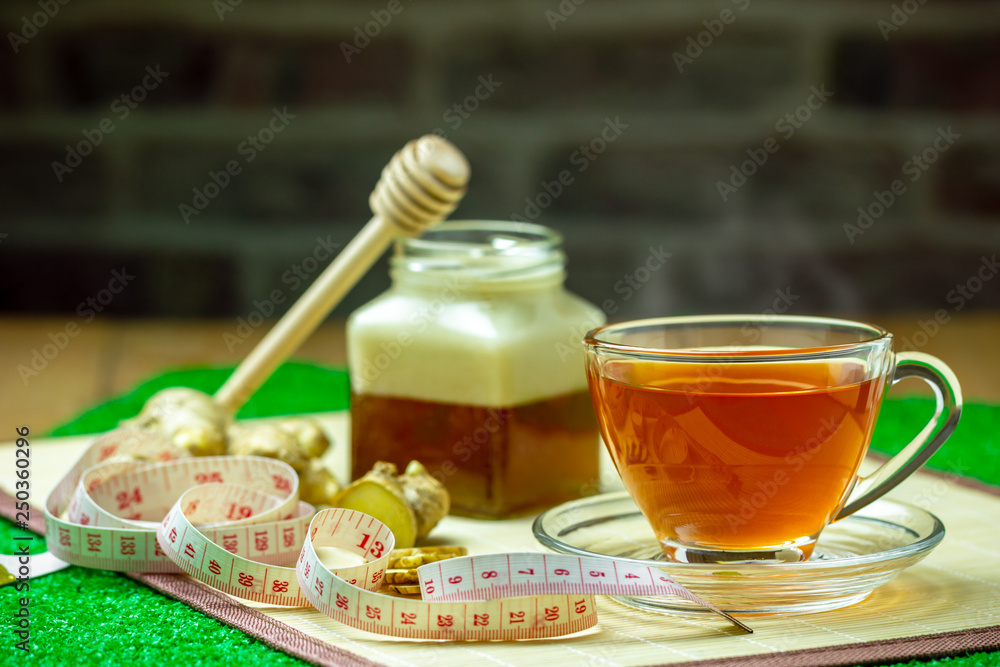 Ginger juice in a clear cup and honey jar placed beside with measuring tape..Concept of healthy. Ginger juice in a clear cup and honey jar placed beside with measuring tape..Concept of healthy.