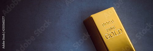 An ingot of gold metal bullion of pure brilliant diagonally located on a blue textured background. photo