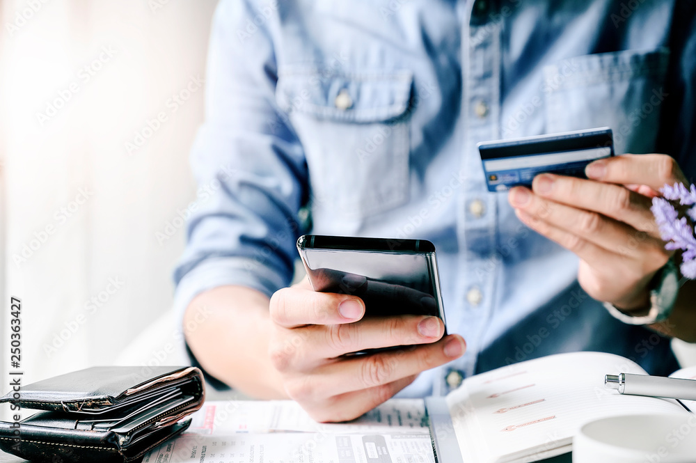 Cropped shot Man paying with credit card on smart phone at home office. Cropped shot Man paying with credit card on smart phone at home office.