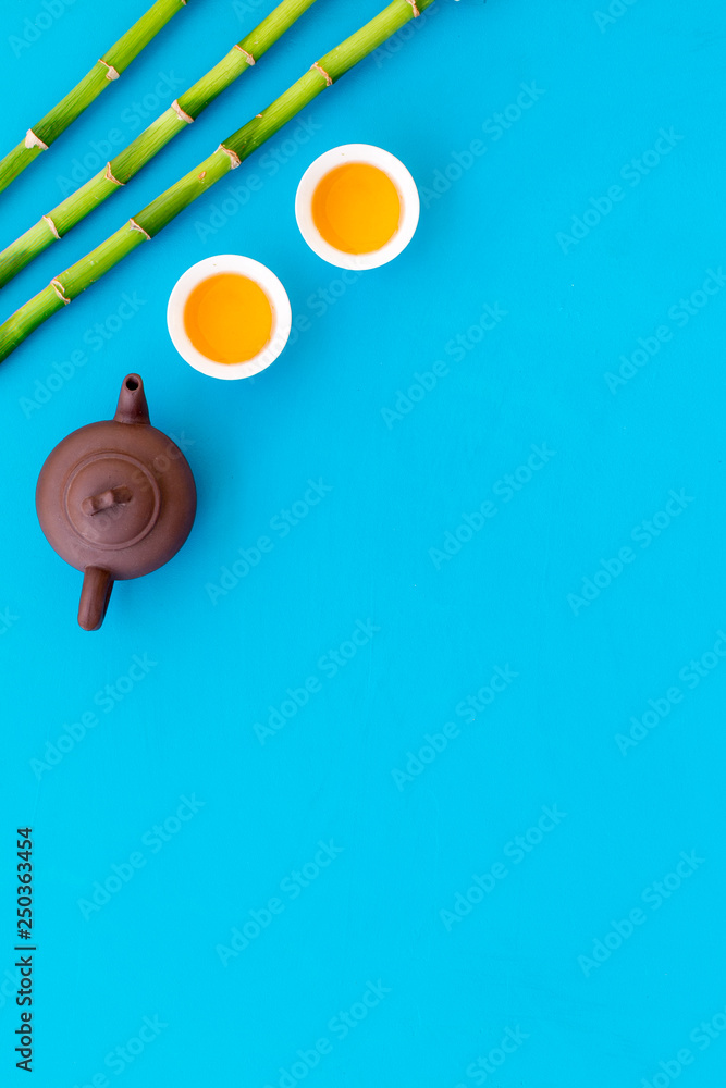 Asian tea traditions. Drink tea. Tea ceremony. Tea pot near cups of green tea and bamboo decoration on blue background top view space for text Asian tea traditions. Drink tea. Tea ceremony. Tea pot near cups of green tea and bamboo decoration on blue background top view space for text