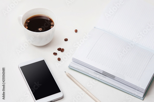 White office desk with blank diary or planner  pencil  phone and cup of coffee. Light background