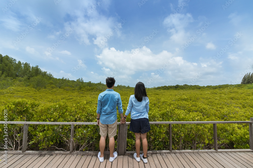 The Asian young couple holding hands on the wooden floor with green trees, blue sky and cloud background. The Asian young couple holding hands on the wooden floor with green trees, blue sky and cloud background.