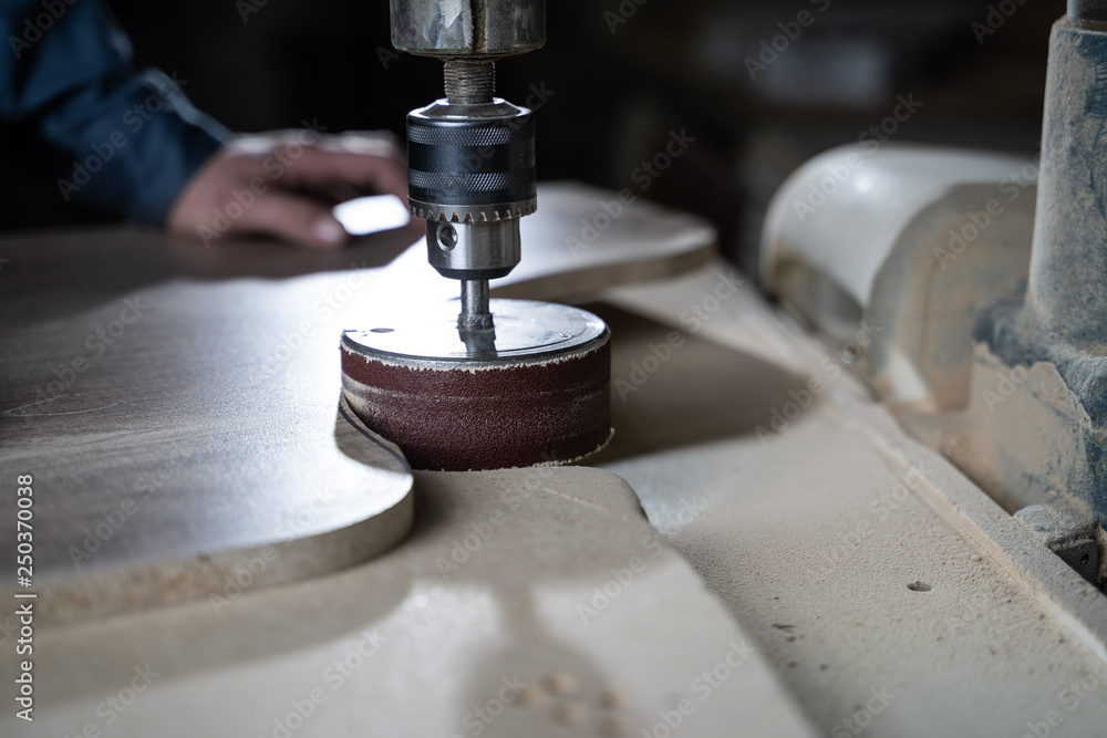 Carpenter polishes a wooden parts on a grinding machine.