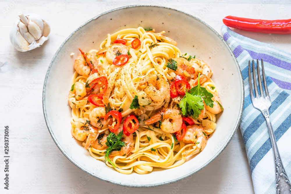 Pasta with shrimps, parsley and chilli peppers on a plate, on a light wooden background - traditional Mediterranean linguine with seafood, Italian cuisine. Pasta with shrimps, parsley and chilli peppers on a plate, on a light wooden background - traditional Mediterranean linguine with seafood, Italian cuisine.