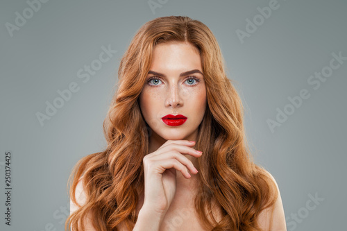 Beautiful model with long curly red hair looking at camera. Wavy shiny hair, perfect face