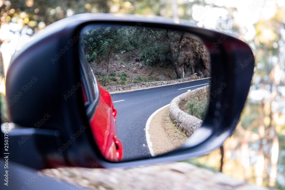  Car driving travel concept - car rear view mirror view of a mountain road with rocks and trees 