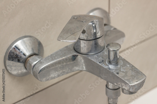 Close-up of shower mixer faucet with limescale, white chalky deposit and stains. Formed on the plumbing system by a combination of soap residues and hard water. Concept of cleaning limescale plumbing