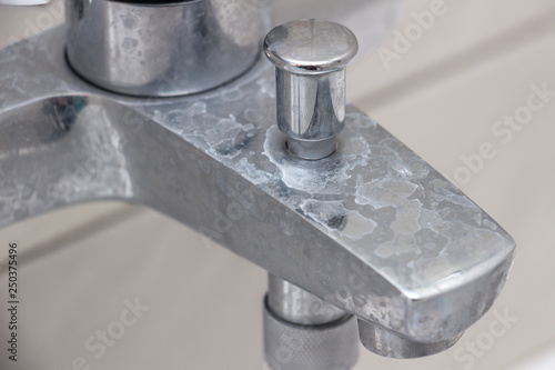 Close-up of shower mixer faucet with limescale, white chalky deposit and stains. Formed on the plumbing system by a combination of soap residues and hard water. Concept of cleaning limescale plumbing photo