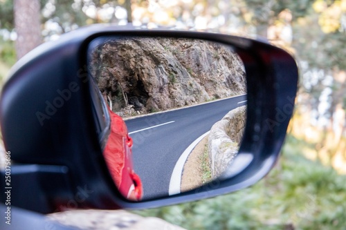  Car driving travel concept - car rear view mirror view of a mountain road with rocks and trees 