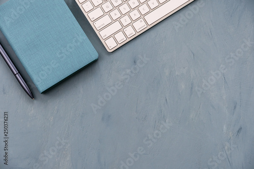 A keyboard, a blue pen and a notebook on a blue desk top.