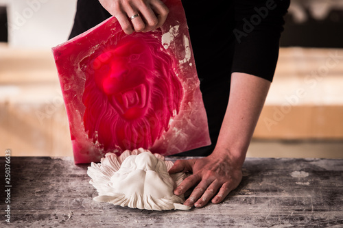 The sculptor works in a plaster workshop. Separates the silicone mold from the plaster sculpture of the lion's head.