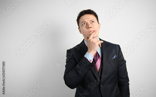 Young businessman in suit on gray background is thinking over question or problem.