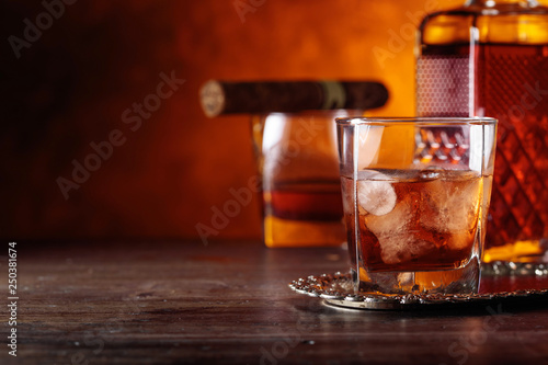 Glass of whiskey and cigar on old wooden table.