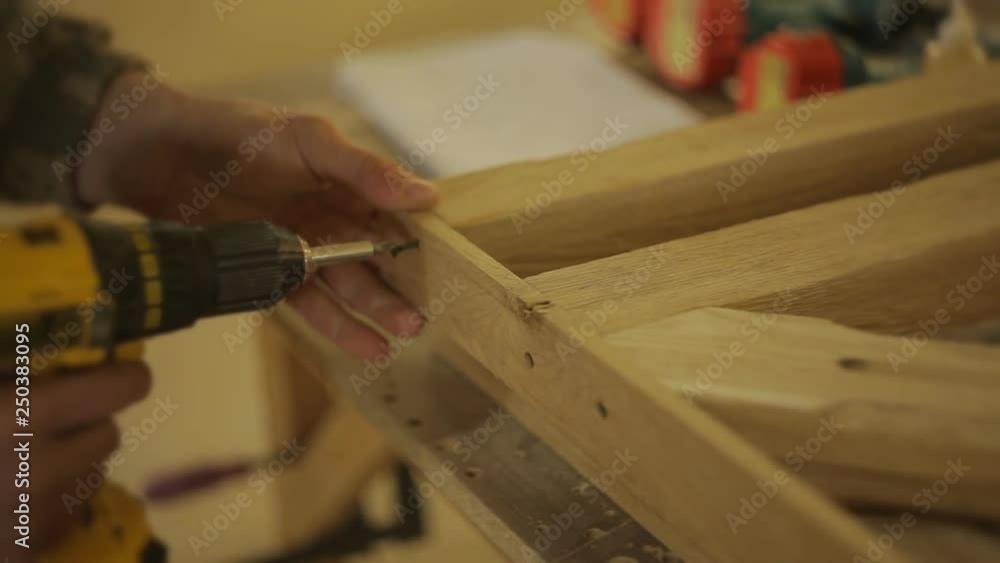 Carpenter or Joiner fastens a wooden product with screw and screw gun or power drill in the furniture workshop Carpenter or Joiner fastens a wooden product with screw and screw gun or power drill in the furniture workshop