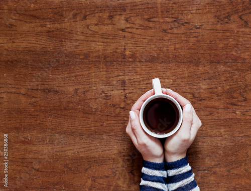 hands holding a cup of coffee on a wooden background