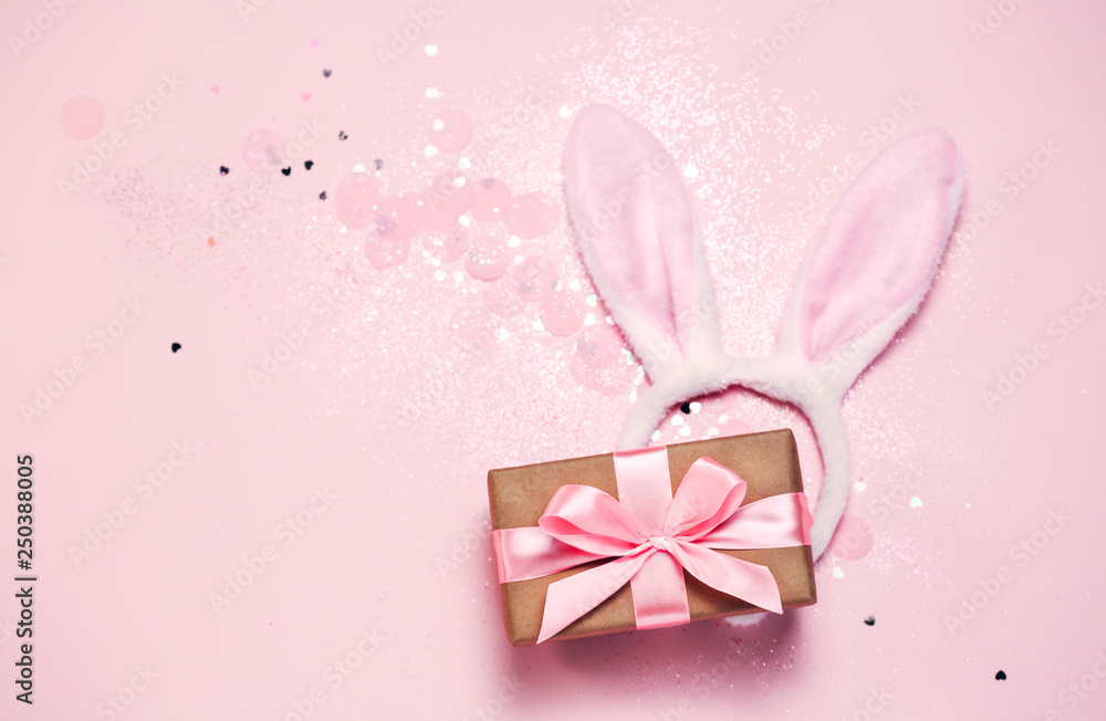 Top view and flat lay of Easter symbol - bunny ears and gift box on pink background. Festive and bright, confetti and sparks. Easter greetings Top view and flat lay of Easter symbol - bunny ears and gift box on pink background. Festive and bright, confetti and sparks. Easter greetings