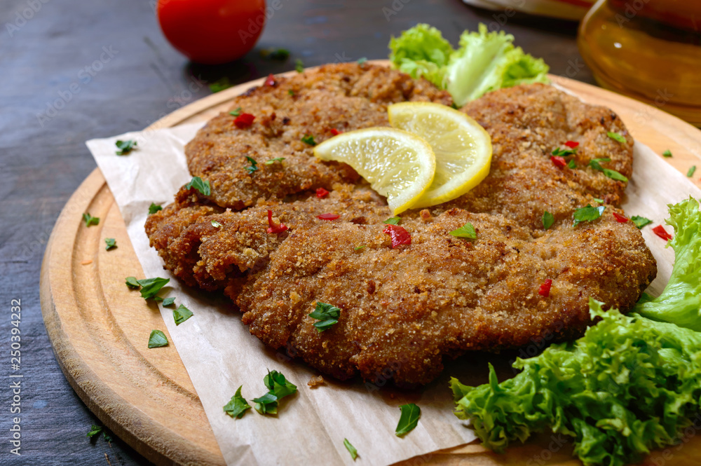 Large Viennese schnitzel on a wooden board with lemon on a dark background. Meat dish