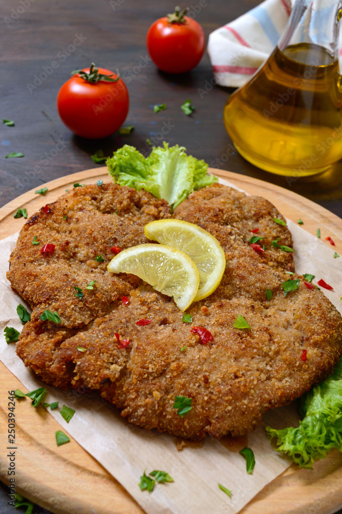 Large Viennese schnitzel on a wooden board with lemon on a dark background. Meat dish Large Viennese schnitzel on a wooden board with lemon on a dark background. Meat dish