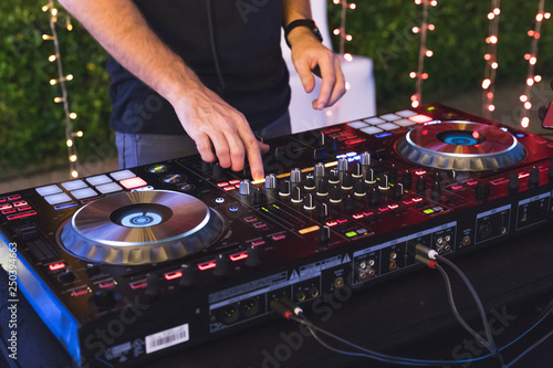 DJ is mixing some music with controller at outdoor night party, by moving hand to set many button