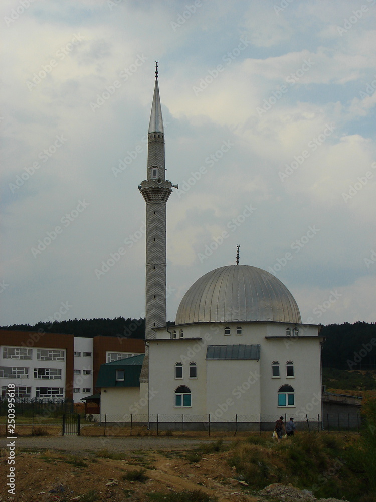Fototapeta premium Mosque in Kosovo, high thin minaret, building next to, cloudy sky