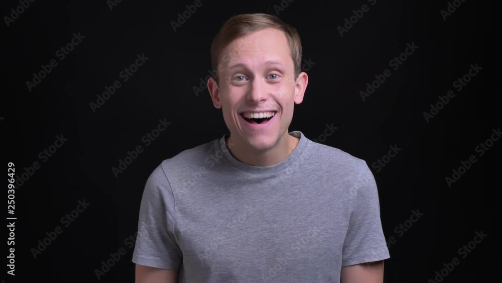 Closeup portrait of young beautiful caucasian man laughing and having fun while looking at camera with background isolated on black Closeup portrait of young beautiful caucasian man laughing and having fun while looking at camera with background isolated on black