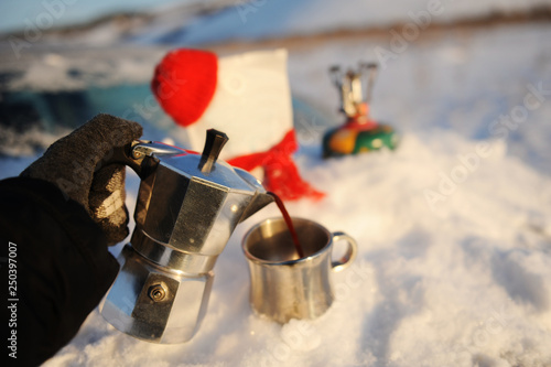 Coffee brewing in moka pot on a gas burner on the car trunk outdoor in winter snow landscape.