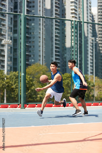young asian adult men playing basketball on outdoor court