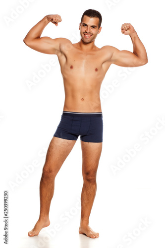 Shirtless handsome smiling man in panties on white background showing his biceps