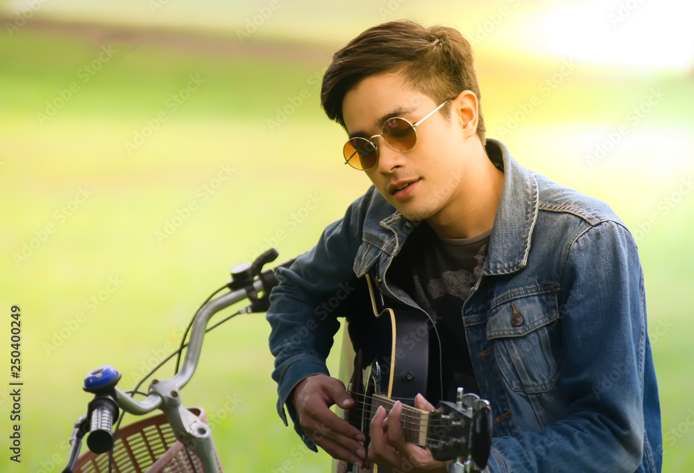 Young man holding a guitar.young men sitting on a bicycle seat  and playing guitar in the park.freedom lifestyle.