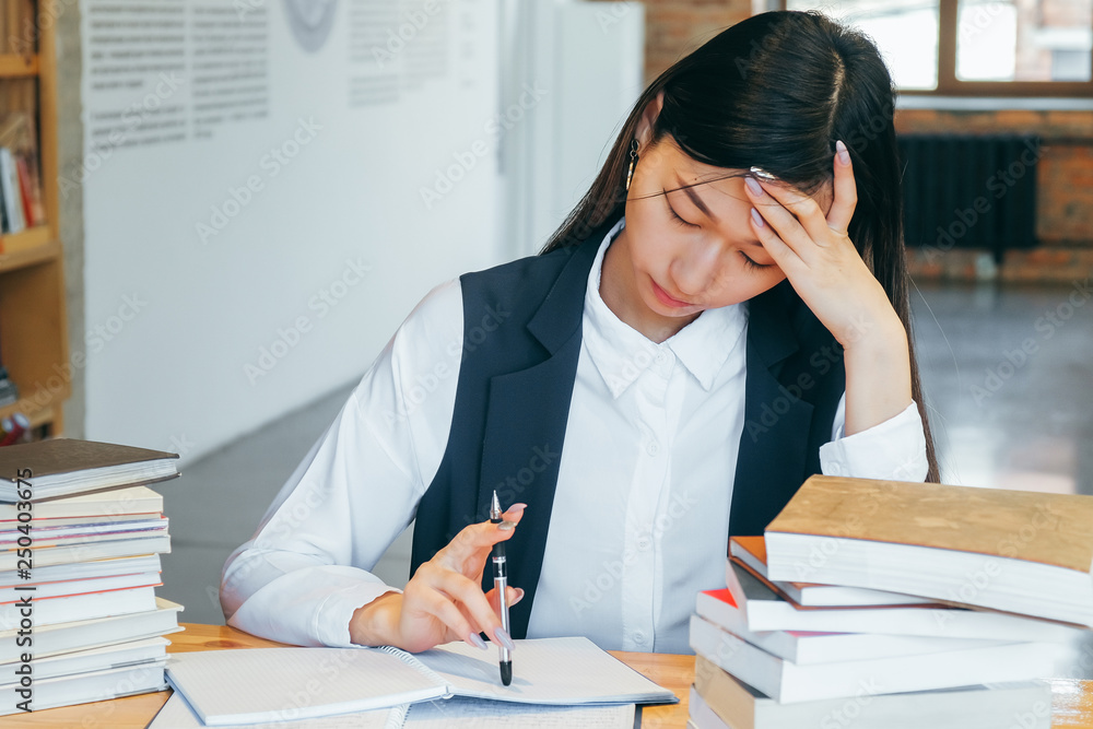 Cute Asian girl sitting in a library, surrounded by books, thinking about studying. Teen student prepares for exams, takes notes and learns. Cute Asian girl sitting in a library, surrounded by books, thinking about studying. Teen student prepares for exams, takes notes and learns.