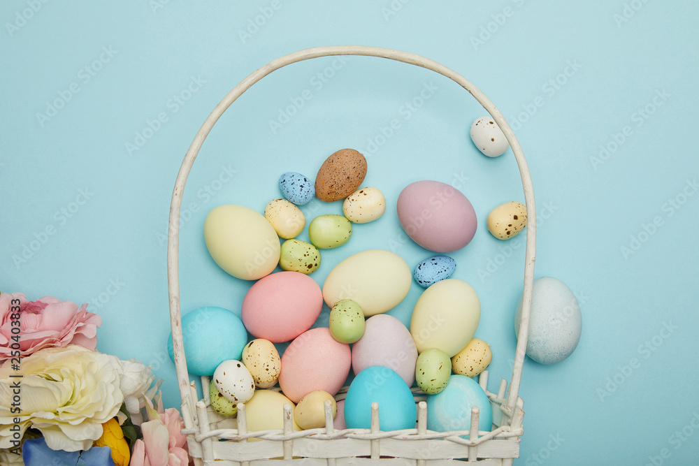 Top view of easter chicken and quail eggs in straw basket and flowers