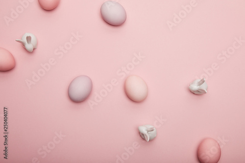 Top view of toy bunnies and painted easter eggs on pink background