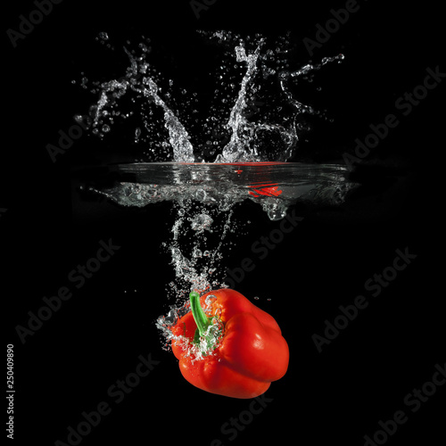Red bell pepper falling in water with splash on black background, paprika, stop motion photography