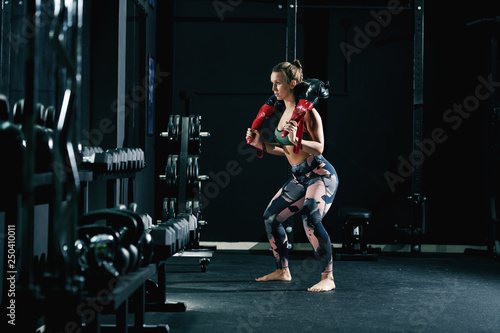 Muscular strong caucasian female bodybuilder in sportswear and with pigtail doing exercises with bulgarian training bag barefoot. © dusanpetkovic1