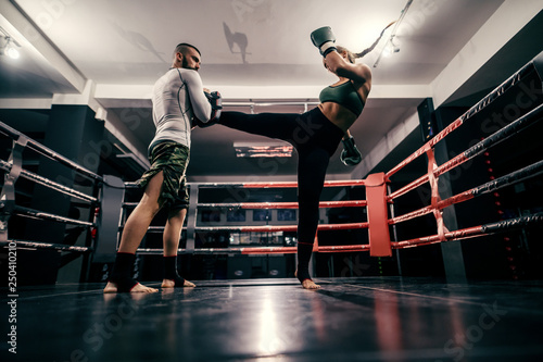 Powerful caucasian boxer girl in sportswear, with bandage on feet and boxing gloves on hands practicing with trainer in ring. © dusanpetkovic1