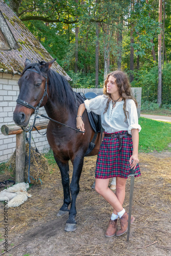Girl in a Scottish kilt standing next to horse holding sword © Andzo Janovich