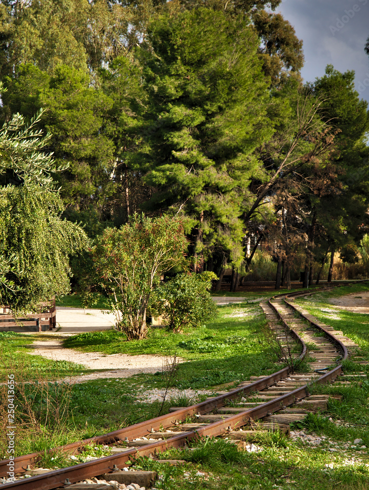 Small railway in a beautiful park with pine and olive trees, in day light. Nice curved line leading in the background. Tritsis park in Athens Greece.
