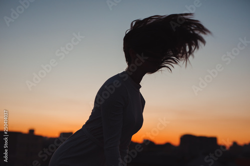 Silhouette of woman toss her hair at sunset in a city