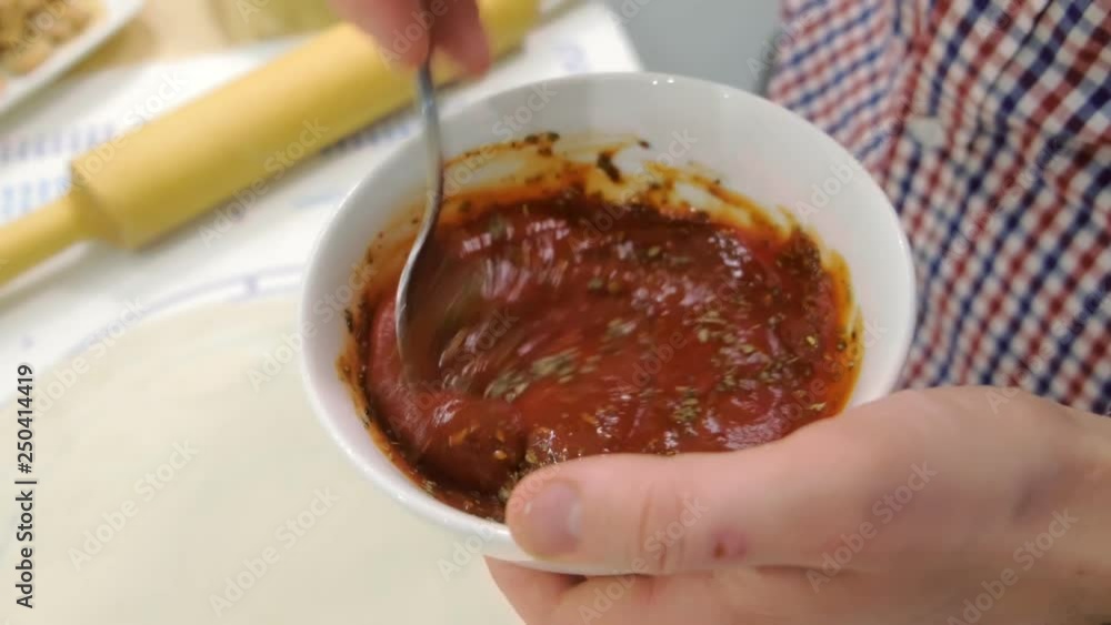 Man mixes tomato sauce with dried Basil in a plate. Sauce for the pizza. Hands close-up. Man mixes tomato sauce with dried Basil in a plate. Sauce for the pizza. Hands close-up.