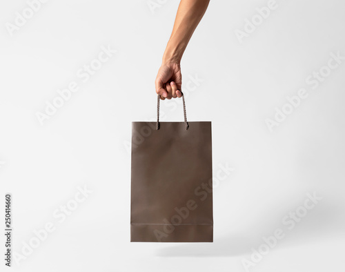 Hand holding blank brown paper bag for mockup template advertising and branding on gray background.